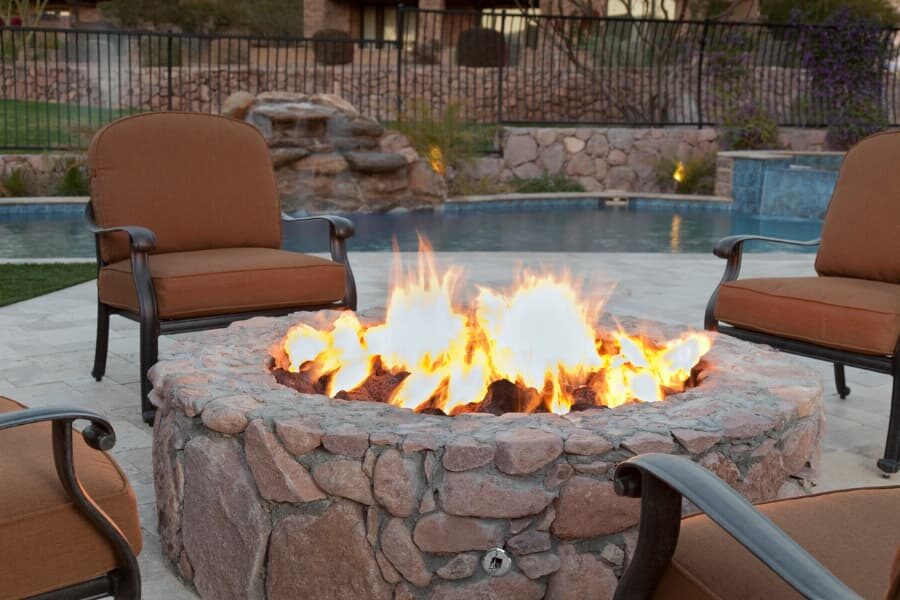 Lit-Stone-Fireplace-With-Chairs-On-Patio-Near-Pool