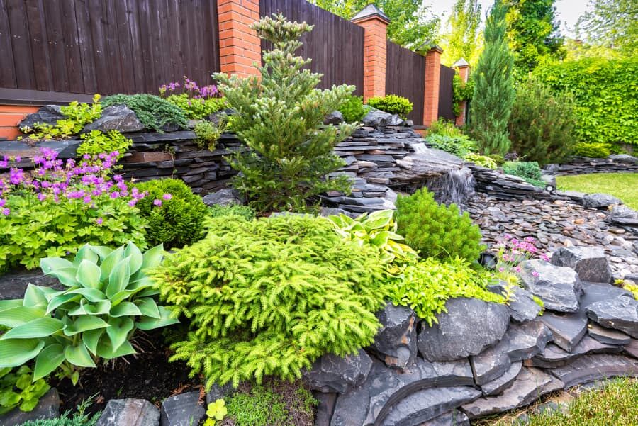 Home garden landscape design with big rocks, plants, flowers, and a small waterfall