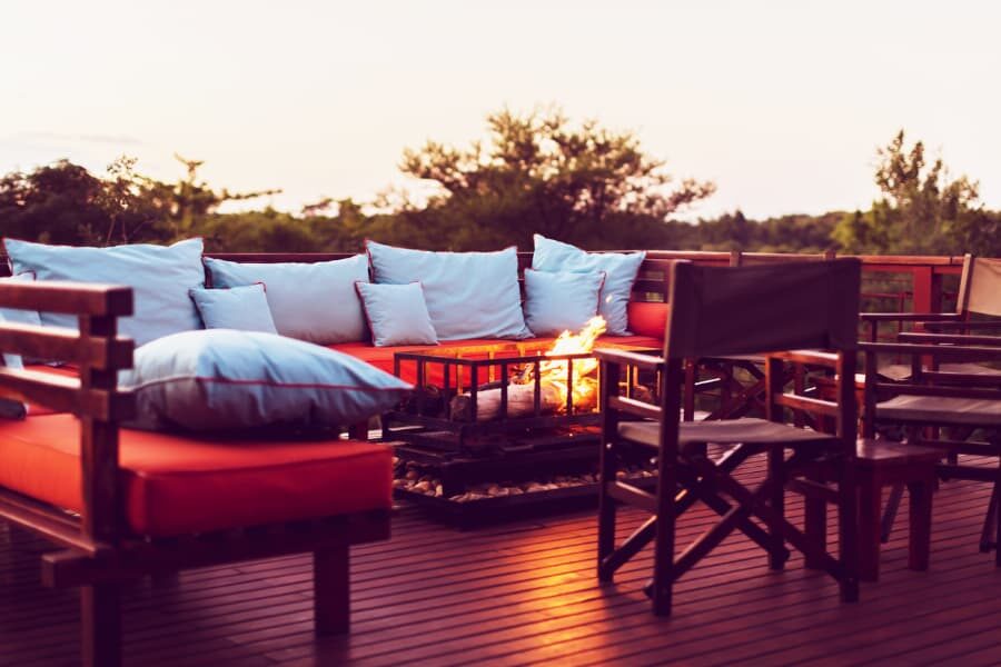 A Beautiful Outdoor Fireplace Situated In The Middle Of A Patio Furniture On A Red Wooden Deck