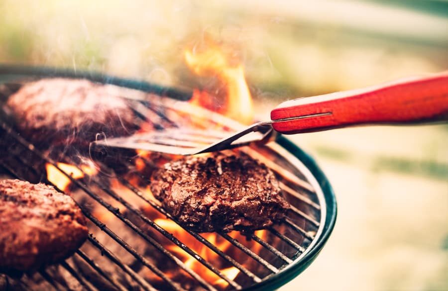 Spatula flipping burgers that are being made on outdoor charcoal grill